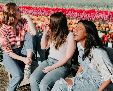 three women sitting wooden bench by the tulip flower field